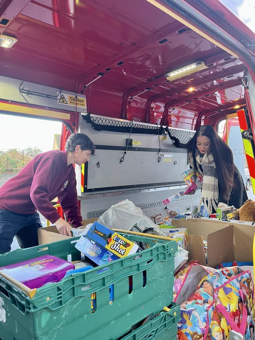 two members of staff stand inside a van with boxes and crates of children's toys