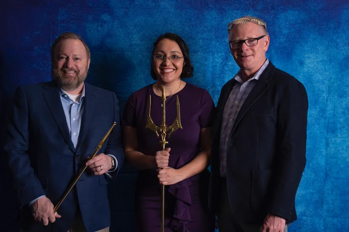 Three people smile and stand in front of a blue background.