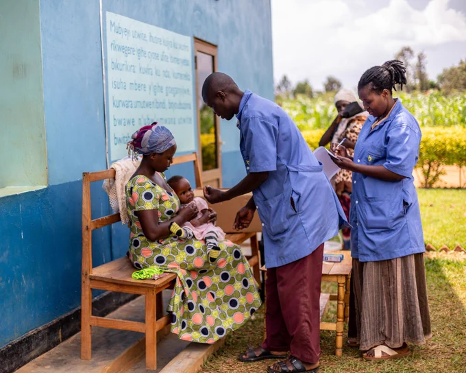 Healthcare workers are attending a baby and a mother seated outside a health facility.