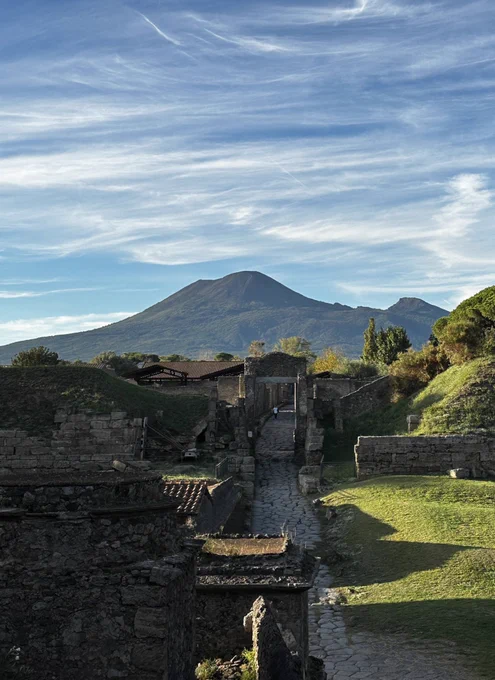 A view up the Roman road that runs under the Nocera Gate with the long shadows falling on vibrant green grass outside the City Walls. In the distance the lush green slopes of Vesuvius.
