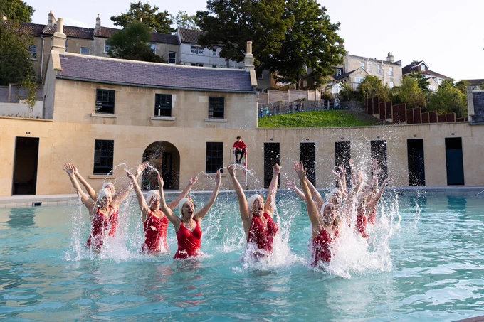 Synchronised swimmers wearing red swimming costumes in the historic pool. Credit: Suzy Slemen