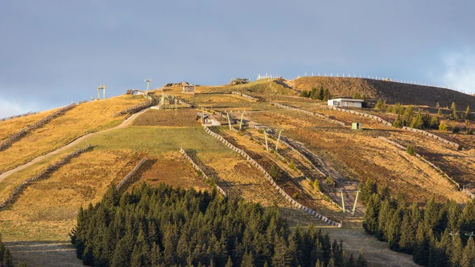 A ski hill pictured with the sun shining on it and no snow