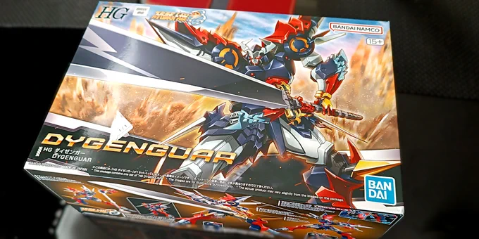 A rather big box on a black table. On the box there's a picture of  Dygenguar, a very intricate robot in black, blue, red and white colors, holding a massive sword and ready to attack.