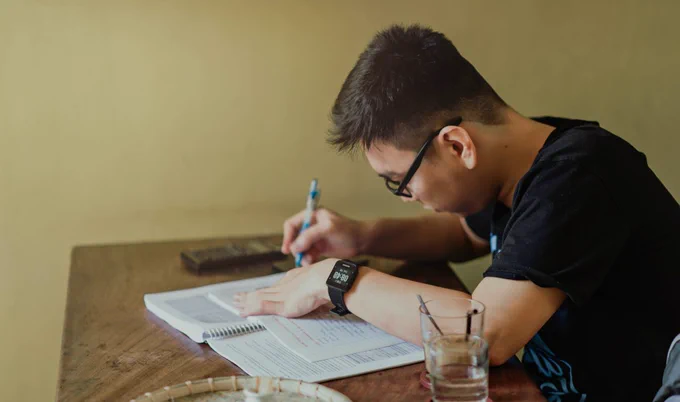 Person sitting on a desk and studying through writing on a notebook.