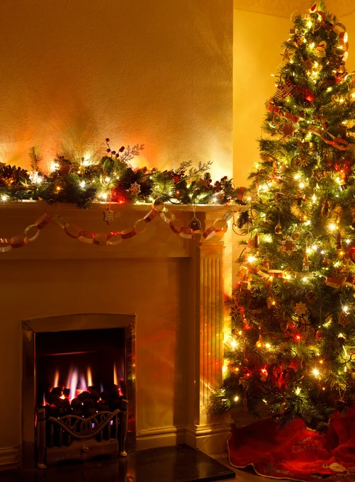 Decorated Christmas tree by decorated mantle over warming fire in fireplace