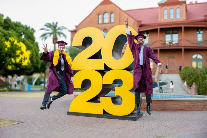 Students jumping joyfully in front of the 2023 sign on the ASU Tempe campus.