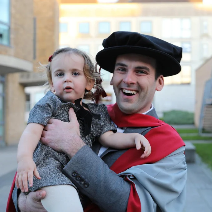 Photo of a graduating student holding his daughter