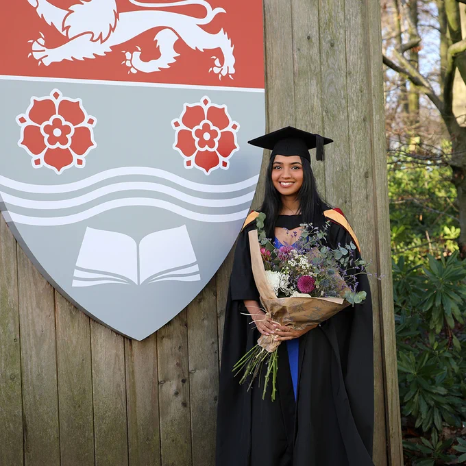 Photos of a graduating student standing next to the Lancaster University crest