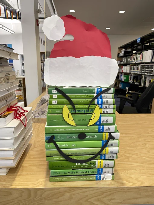 A pile of books with green jackets piled on top of one another with the face of the grinch on it and a Santa hat on top