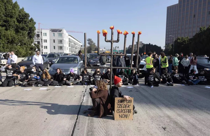 Picture of protestors seated on freeway, blocking cars, with a large menorah in front of them