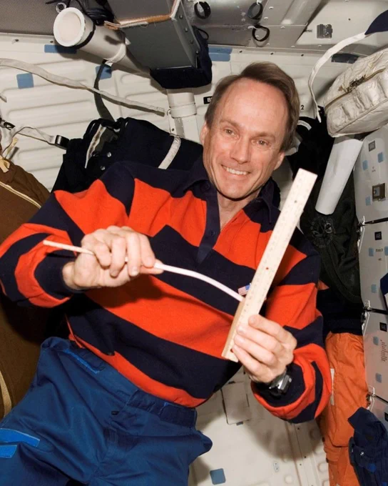 Dr. Steve MacLean surrounded by various floating objects in microgravity.
