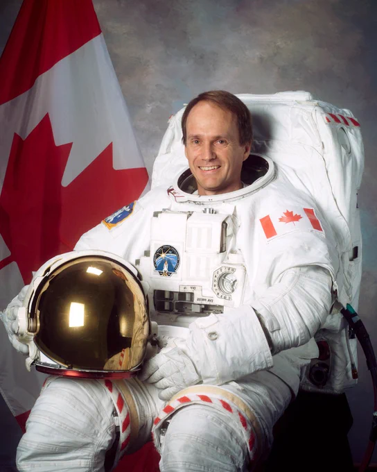 Dr. Steve MacLean in a white spacesuit with a Canada flag in the background. 