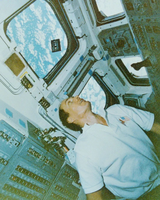 Dr. Steve MacLean aboard Space Shuttle Columbia.  We can see clouds outside the window. 