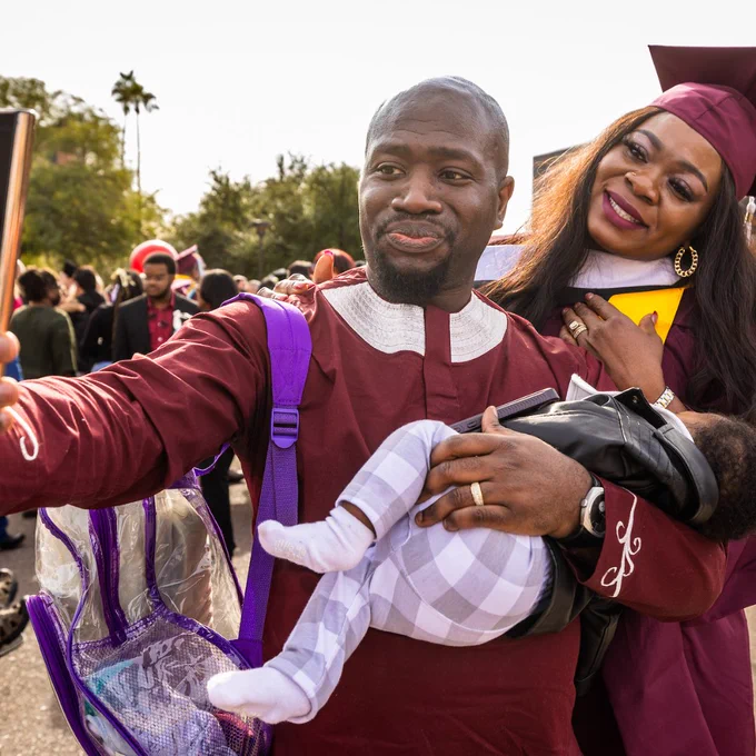 Graduates embrace and hold a baby outside of Desert Financial Arena as they take a selfie
