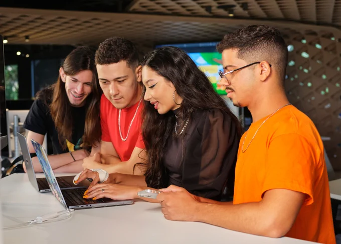 Four students huddled together around a desk in Brazil, working together on a MacBook.
