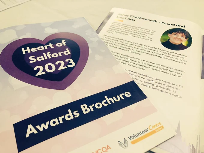 Two flyers on a table. The first flyer is in focus and reads: 'Heart of Salford 2023 Awards Brochure in graphic text'