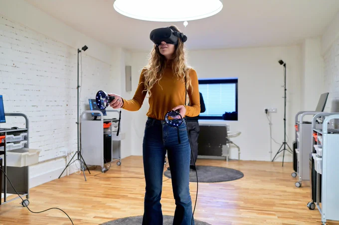 A woman stands in a learning space using a virtual reality headset and controllers.