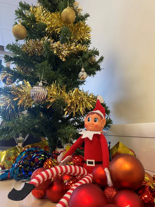 elf sat in baubles next to a Christmas tree