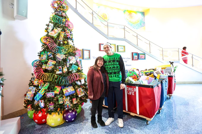 Jason and his mom pose for a picture in front of the toys and the Christmas tree