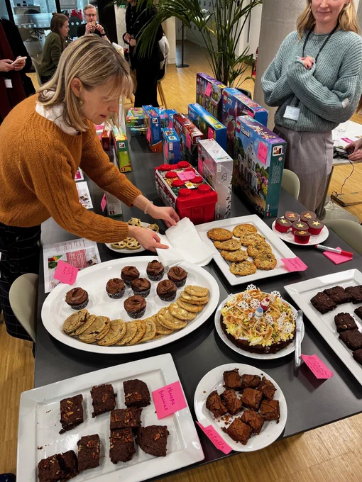 A woman takes a napkin at a stand selling cakes, biscuits and boxed LEGO sets.