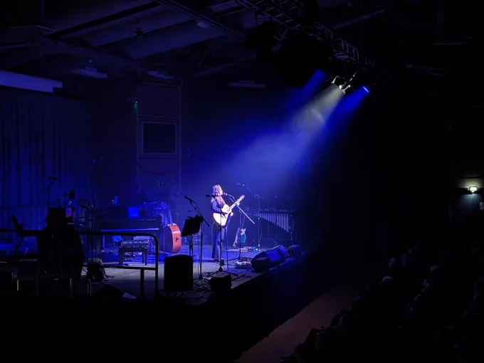 Katherine Priddy onstage at the Sheffield Octagon, singing and playing guitar, lit in blue and white.