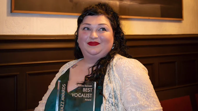 A picture of a woman wearing red lipstick and looking off to the right. She is holding a Scottish Jazz Awards award plaque for Best Vocalist Award