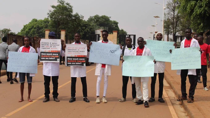 Scientists in white lab coats and other activists from SR Uganda hold placards in a road. How much more climate failure will we take?