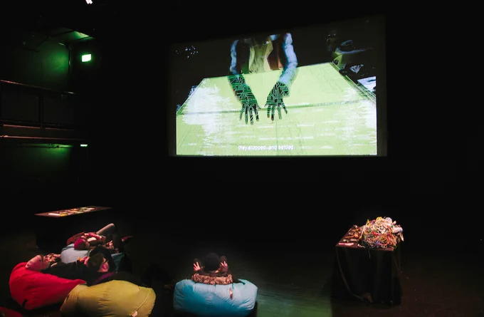 People lying on beanbags watching a projection of hands working on a circuit board with subtitles that read "they stopped and settled".