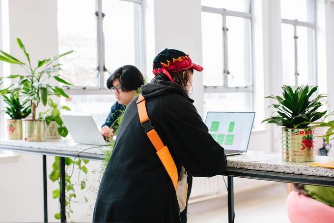 Two people standing looking at laptops, surrounded by potted plants