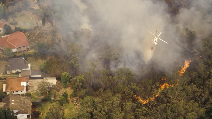 A water bomber plane flies over a forest fire as it burns near a residential area
