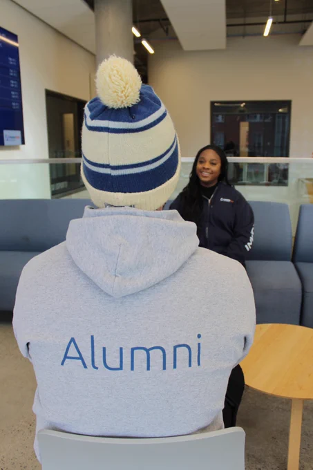 photo of person talking to woman wearing alumni merch 