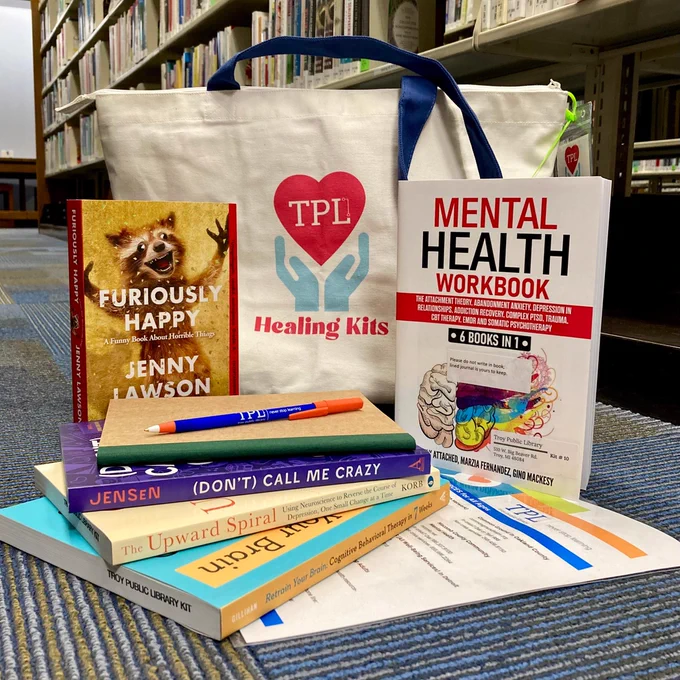 Healing Kits tote bag in book aisle with mental health books, resource list, and journal and pen