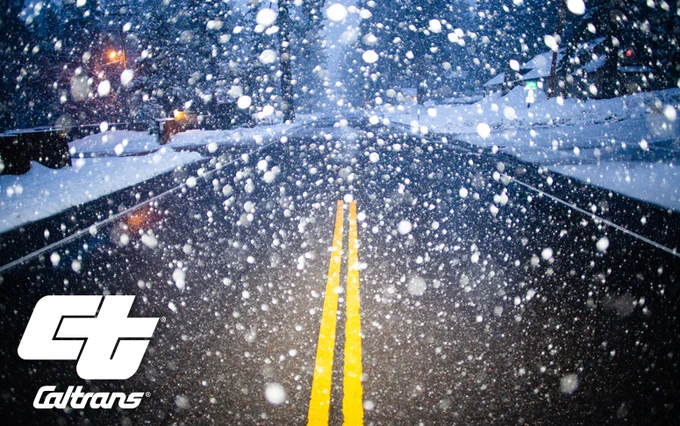 Empty road viewed through a windshield of a car, with snow heavily falling. Caltrans logo in the corner. 