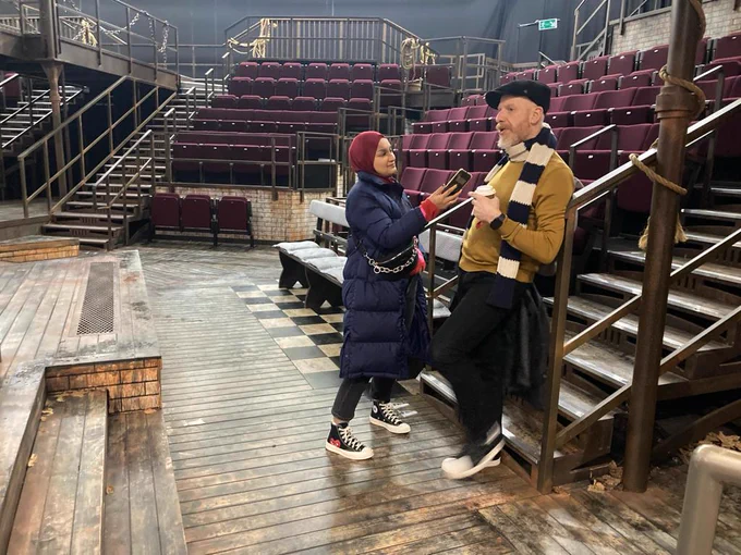 Two people in the Quarry theatre at Leeds Playhouse. There is no audience and they are standing by the stage. One is holding a microphone and looks like they're interviewing the other.