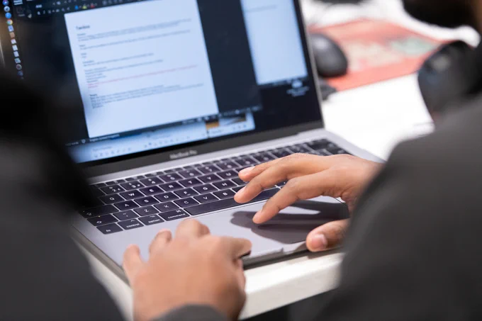 A close up photo of some hands typing at a laptop keyboard