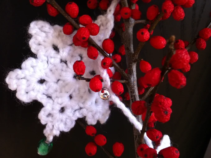 Branch of red berries entwined in a white crochet start garland