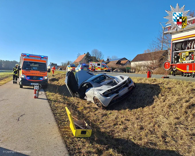 Zeigt den verunglückten McLaren. Im Hintergrund sind Fahrzeuge des Rettungsdienstes, der Feuerwehr und der Polizei zu sehen. 