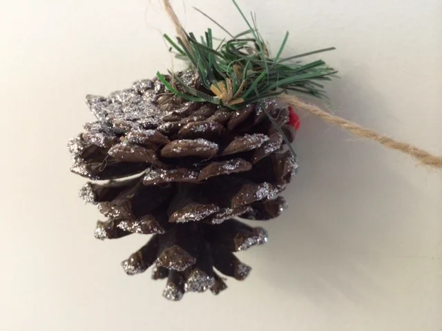 Close up photo of a pinecone christmas decoration with green trim, hanging from string