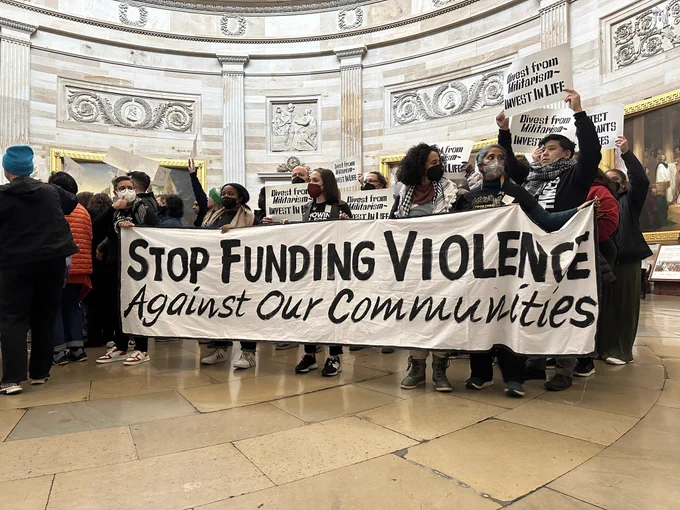 Photo of people holding a banner that says “stop funding violence against our communities”