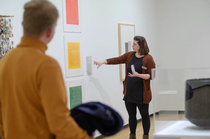 A woman points toward prints that are arranged in a red-yellow-green stoplight pattern in an art gallery.