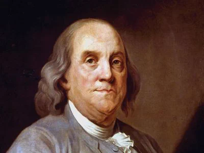 An image depicting Benjamin Franklin wearing a grey 18th-century era shirt. 