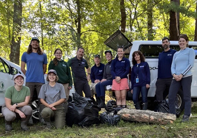 A group of people post with a large, full trash bag.