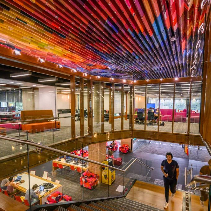 Inside QUT Kelvin Grove Library taken from the top of the stairs looking down to the bottom level and featuring the books artwork on the ceiling and a student walking up the stairs. 