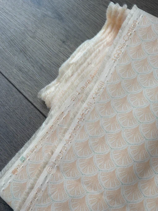 Folded fabric on the floor. It is orange and blue and is covered in little fans. The selvage edge shows the words “Laura Ashley MCMLXIII”