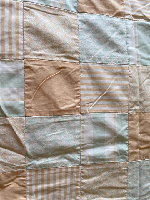 A close up of a pastel orange and blue baby quilt. One of the squares has the exact same pattern on it as the first photo.