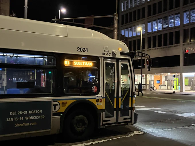 MBTA bus 2024, operating Route 91 toward Sullivan, enters an intersection at night with its headlights on.