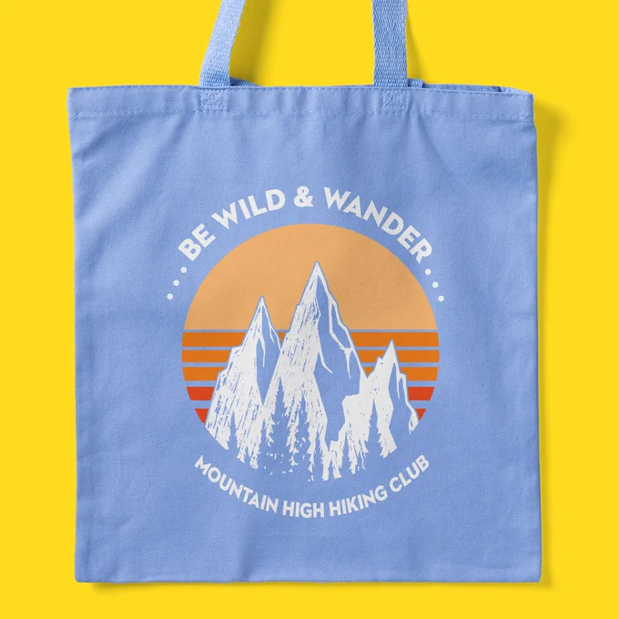 Sky blue tote bag with mountain design. Text around it reads "Be Wild & Wander. Mountain High Hiking Club."