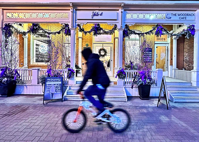 Street scene of old building with veranda decorated with purple Christmas decorations. A man with a bike rides in front on the sidewalk