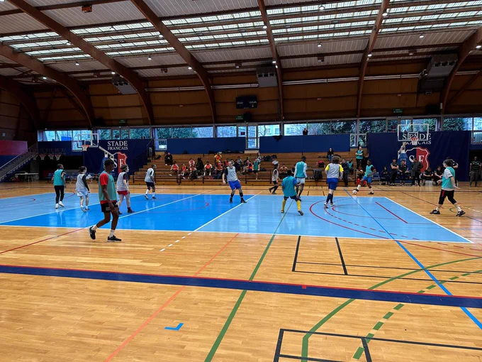 Joueurs en mouvement pendant un match du trophée du vivre ensemble. Prise de vue large du terrain.