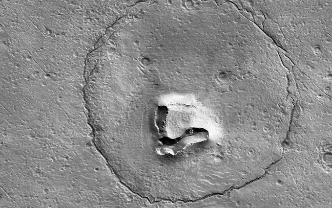 A V-shaped collapse structure makes the nose, two craters form the eyes, and a circular fracture pattern shapes the head.